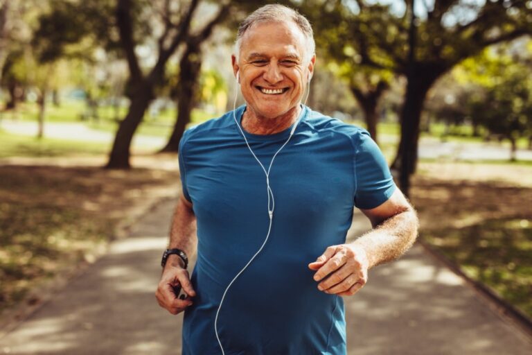 A man smiling running along an outdoor path while listening to headphones