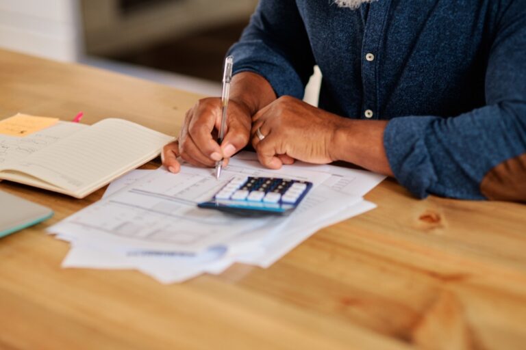 A person sitting at a table with a calculator, pen, and papers