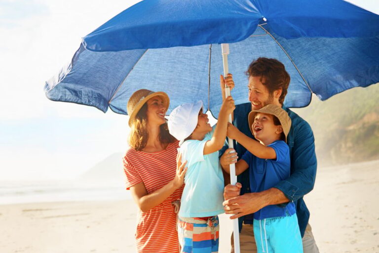 Young mother, two sons and father under blue beach umbrella